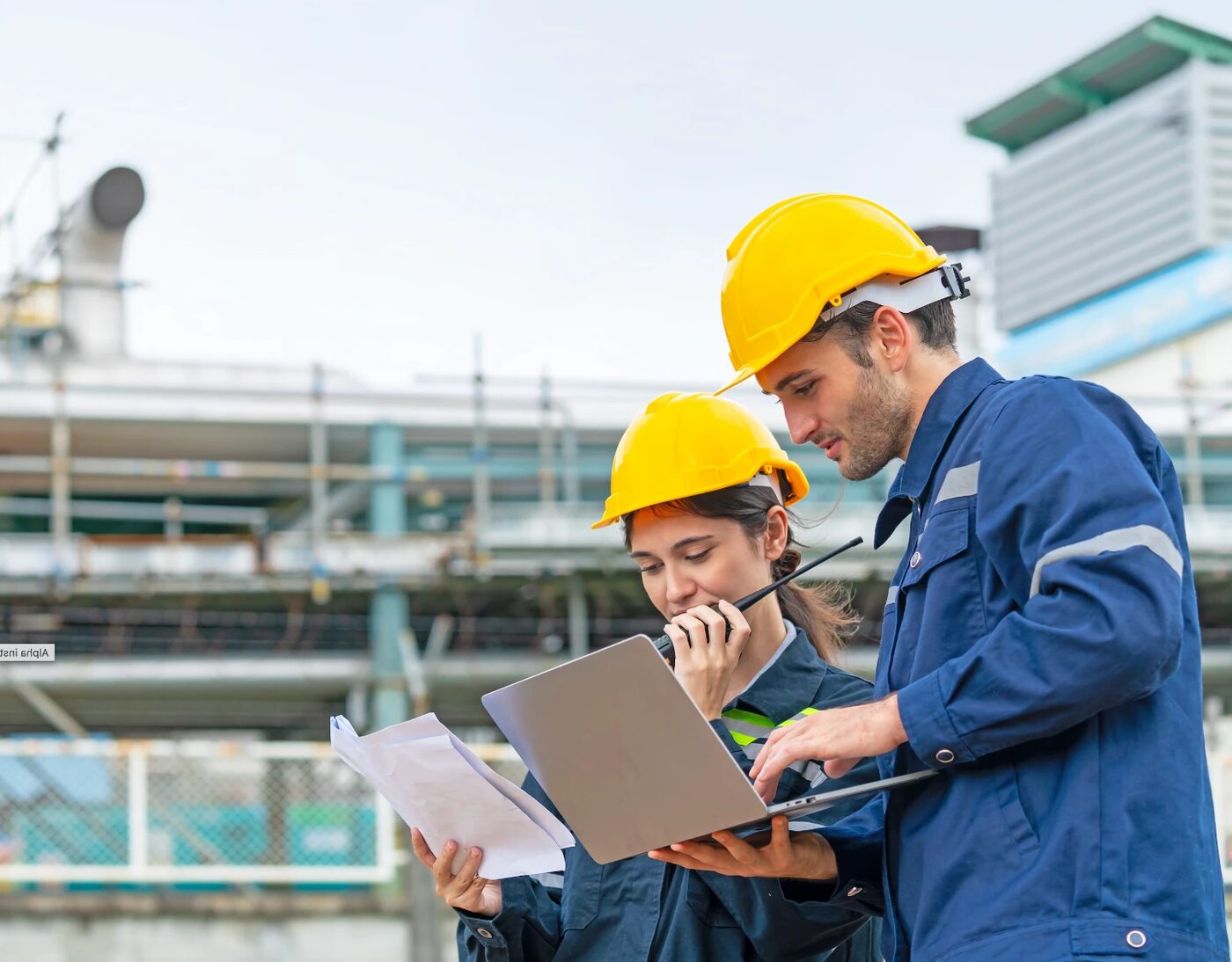 Un technicien et une technicienne en casque de chantier consultent des plans devant une installation industrielle