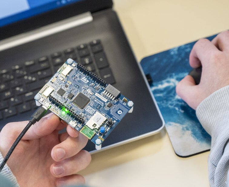 Mains tenant une carte électronique devant un ordinateur portable
